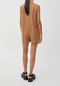 Combinaison brune sans manches avec un col, un tissu texturé et une coupe ample. Sandales à plateforme noires avec des sangles ajustables.