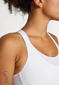 Hvit atletisk tanktopp med rund hals og tynne stropper, laget av et glattholdig, elastisk stoff. Har et tettsittende design.