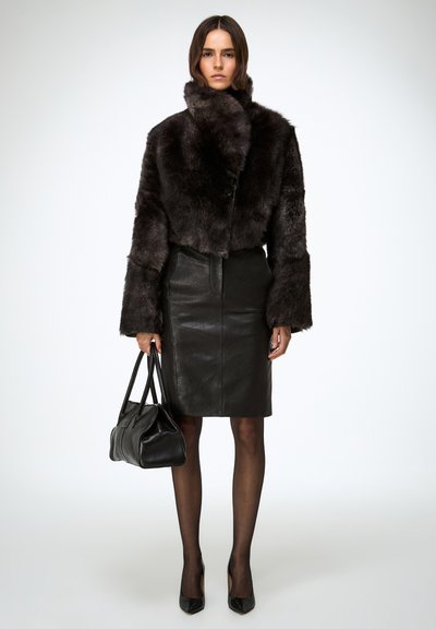 Crna jakna od lažnog krzna kratkog kroja s širokim rukavima, uparena s crnom kožnom olovka suknjom. Drži crnu kožnu torbu, nosi crne cipele na petu.