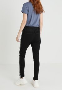 Zwarte sportbroek met een taps toelopend ontwerp, zijstrepen in het wit en een elastische tailleband, gecombineerd met een grijs T-shirt met korte mouwen en witte sneakers.