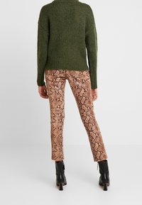 Grüner, grob gestrickter Pullover, braune Schlangenhautmuster-Schlupfhose in Slim-Fit, schwarze Stiefeletten mit Blockabsätzen, sichtbaren Nähten und strukturiertem Stoff.
