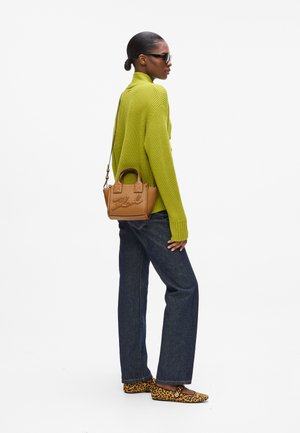 Woman wearing a green turtleneck sweater, dark blue jeans, leopard print flats, black sunglasses, and carrying a small brown handbag on her shoulder.