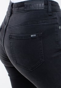 Vaqueros de mezclilla negra con una vista en primer plano del bolsillo trasero, que presenta una etiqueta "BIG STAR" y detalles de costura únicos. Textura suave.
