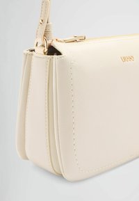 Borsa a mano in pelle beige chiaro con un design strutturato, dotata di chiusura con zip dorata, dettagli cuciti e tracolla rimovibile.