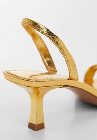 Gold metallic high-heeled sandals with a sleek strap design, featuring a glossy finish, contoured footbed, and a square-shaped heel.
