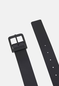 Curea din piele neagră, cu o cataramă pătrată din metal negru și logo gravat. Prezintă o textură netedă și multiple găuri de ajustare pentru a se potrivi mărimii.