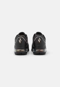 Black athletic shoes featuring a textured upper, cushioned heel with a transparent air unit, and metallic rose accents on the back.