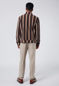 Brun och krämfärgad vertikalt randig skjorta med krage, matchad med ljusbeiga byxor och svartrandiga skor.