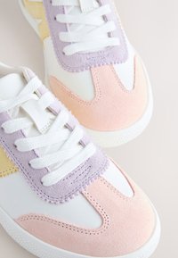 Baskets blanches avec des touches de daim pastel rose, lavande et jaune, lacets blancs et semelles en caoutchouc texturées.
