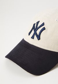 Căciulă de baseball din catifea, cu secțiune superioară crem și vizieră bleumarin. Logo-ul brodat NY în bleumarin pe față.