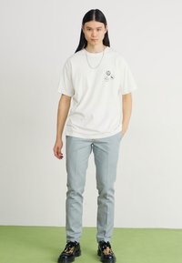 Tricou alb din bumbac cu trei pete negre circulare; asortat cu pantaloni albastre deschise, ajustați, și teniși negri cu detalii în imprimeu de leopard.