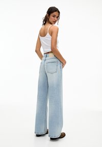 Hellblaue weite Jeans mit hoher Taille, ausgestattet mit Gesäßtaschen, einem hellbraunen Lederpatch am Bund und einem fransigen Saum.