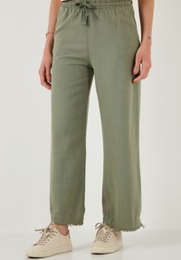 Hellgrüne, locker sitzende Hose mit elastischem Bund, Zugbanddetails und ausgefranstem Saum. Aus weichem, strukturiertem Stoff gefertigt.