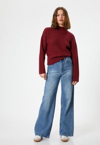 Sweter w kolorze wina z prążkowanej tkaniny, z długim rękawem, zestawiony z jasnoniebieskimi spodniami o szerokich nogawkach i białymi trampkami. Prosty design, casualowy krój.
