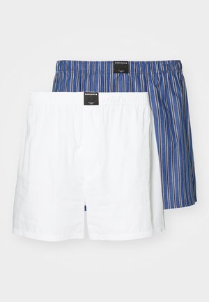 Zwei Paare Boxershorts: eine einfarbig weiß, die andere blau mit weißen vertikalen Streifen. Beide haben elastische Taillenbündchen und Stoffetiketten.