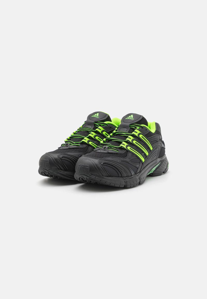 Zapatillas deportivas negras con acentos en verde neón, parte superior de malla texturizada, suela acolchada y un sistema de cordones distintivo.