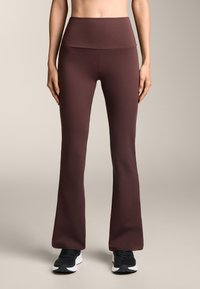 Legginsy z wysokim stanem i rozszerzanym dołem w ciemnym burgundowym kolorze, charakteryzujące się gładką teksturą i bezszwowym designem. W zestawie z czarnymi butami sportowymi.