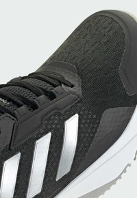 Zwarte sportschoen met een bovenwerk van textuurstof, zilveren drie-strepen ontwerp en een witte rubberen zool met een duidelijk profielpatroon.