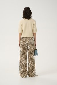 Cream short-sleeve sweater paired with wide-leg leopard print trousers. Model holds a small blue handbag with a gold handle.