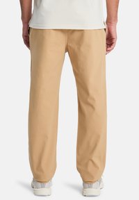 Beige katoenen broek met een relaxte pasvorm, rechte pijpen en zonder zichtbare patronen. Gekoeld met lichtgrijze sport schoenen.