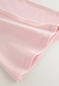 Primo piano di tessuto a coste rosa chiaro con orlo ripiegato e cuciture visibili su una superficie bianca.