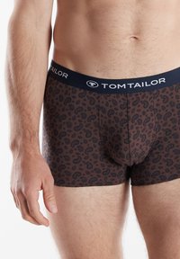 Brown boxer briefs featuring a black paisley pattern. The waistband is navy blue with the brand name "TOM TAILOR" in white lettering.