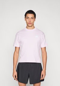 Hele roosa puuvillane T-särk ümmarguse kaelusega, lühikeste varrukatega ja väikese sinise logoga rinnal, kombineeritud mustade lühikestega.