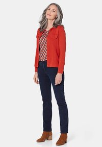 Rode button-up jasje met twee borstzakken, geprint top, donkere spijkerbroek en bruine suède enkellaarsjes met een blokhak.