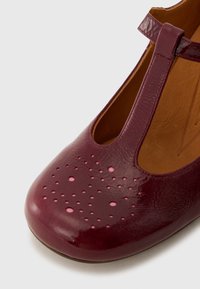 Scarpa in pelle bordeaux con dettagli perforati sulla punta, design a T, finitura lucida e fodera interna marrone. Forma della punta rotonda.