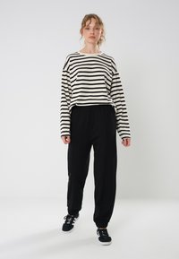 Svart og hvitstripete langermet topp kombinert med svarte joggebukser. Har avslappet passform og ribbestrikkede mansjetter. Svarte sneakers fullfører antrekket.