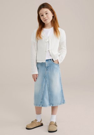 Fehér kötött kardigán nyitott mintával, világoskék denim midi szoknyával párosítva, bézs slip-on cipőkkel és fehér bokazoknival.