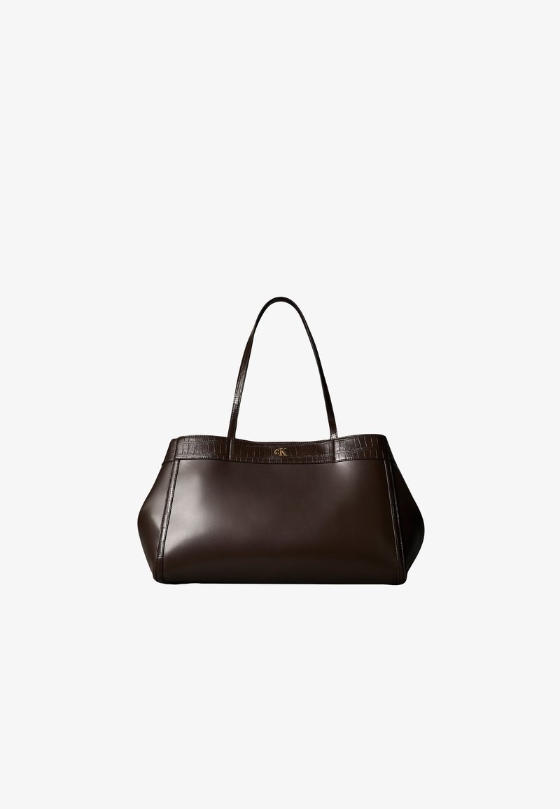 Sac à main en cuir brun foncé avec un corps lisse, une bordure texturée crocodile, deux poignées et un petit logo doré "cK" sur le devant.