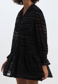Svart klänning med genomskinligt, randigt tyg, knappslå, elastiska ärmar och utsvängd kjol. Har en volangslutning och avslappnad passform.