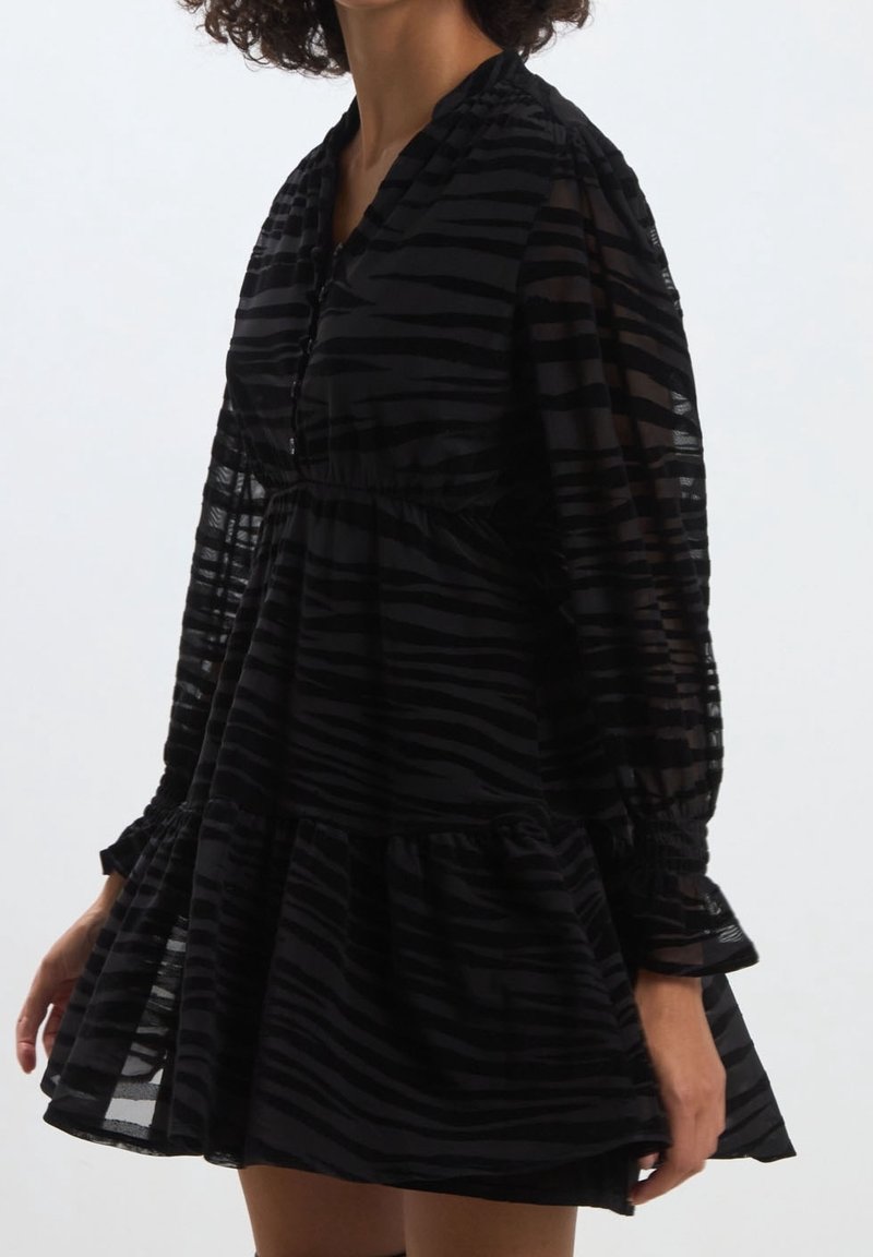 Svart klänning med genomskinligt, randigt tyg, knappslå, elastiska ärmar och utsvängd kjol. Har en volangslutning och avslappnad passform.