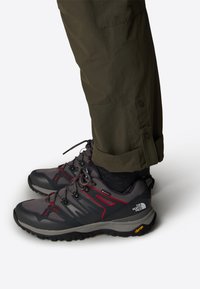 Harmaat vaelluskengät punaisilla yksityiskohdilla, teksturoitu verkko-etuosa ja kumipohja. Yhdistetty oliivinvihreisiin housuihin. Vibram-logot pohjassa.