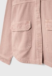 Giacca di denim rosa chiaro con chiusura a bottoni, due tasche frontali con alette appuntite e collo strutturato. Tessuto liscio.