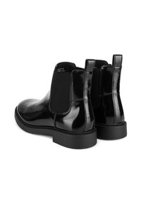 Cizme Chelsea din piele lucioasă neagră, cu panouri elastice pe laterale și cu bucle pentru a fi mai ușor de încălțat. Prezintă vârful rotund și o talpă joasă din cauciuc texturat pentru aderență.