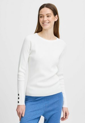 Pull en maille côtelée blanche à manches longues avec un col rond et des accents de boutons sur les poignets, associé à un pantalon bleu. Texture lisse, coupe ajustée.