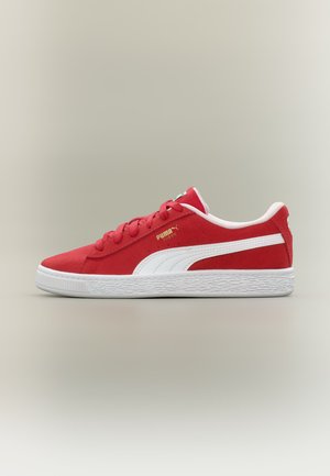 Baskets Puma en daim rouge avec bande logo Puma blanche, semelle blanche et lacets rouges sur fond neutre.