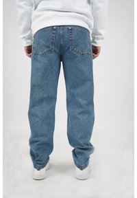 Světlé modré volné džíny s vysokým pasem, pěti kapsami a měděným kováním, doplněné bílými teniskami.