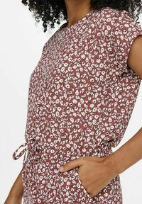 Bluse mit floralem Druck in rostrot, kurzen Ärmeln, lockerem Schnitt und Kordelzug in der Taille; weist weiße und hellblaue Akzente im Muster auf.