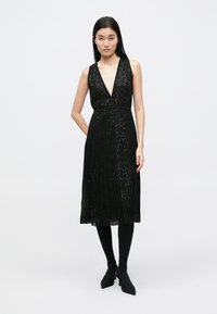 Fekete ujjatlan ruha mély V-nyakkivágással, flitterekkel díszítve, testhezálló felsőrésszel és térdig érő, pliszírozott szoknyával.
