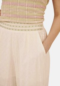 Top de punto a rayas en rosa claro y crema con un patrón texturizado, combinado con pantalones anchos de talle alto en beige que tienen bolsillos laterales.