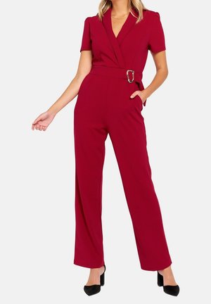 Bordowy kombinezon z krótkimi rękawami, zapinany z przodu, z paskiem w talii ozdobionym srebrną klamrą oraz szerokimi nogawkami.