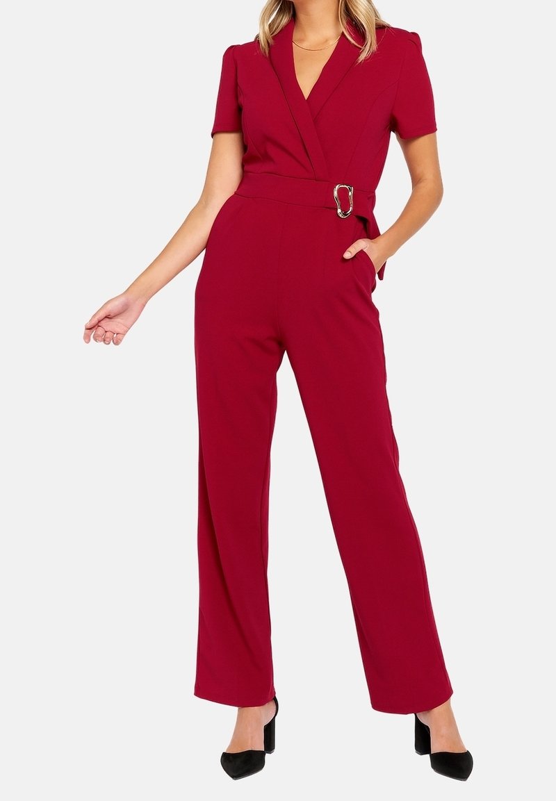 Combinaison bourgogne à manches courtes, design à devant croisé, taille ceinturée avec boucle en argent, et pantalon large.