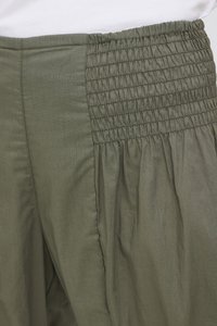 Pantaloni verde măsliniu cu detaliu de smoc elastic adunat la talie, văzuți în prim-plan pe zona superioară a șoldului.