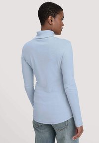 Lichtblauw langemouwen turtleneck shirt gemaakt van zachte, gladde stof. Heeft een aansluitende pasvorm en een gebogen zoom, gecombineerd met losse jeans.
