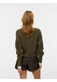 Maglione lavorato a maglia verde oliva con design corto, spalle scese e tessitura a coste, abbinato a pantaloncini in pelle nera.