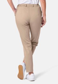 Pantalons tapered beiges en tissu flexible, avec une taille élastique et de petites plissures, associés à des chaussures de sport blanches.