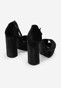 Tacones de plataforma negros con textura de terciopelo, que cuentan con un alto tacón cuadrado y un diseño de punta abierta. Correa ajustable en la parte posterior.